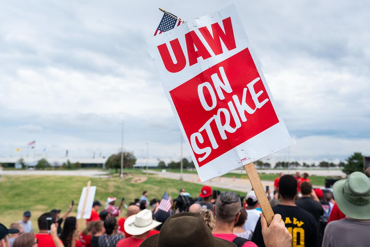 Bild på folk på strejk med en person som håller upp en skylt med texten "UAW on strike"