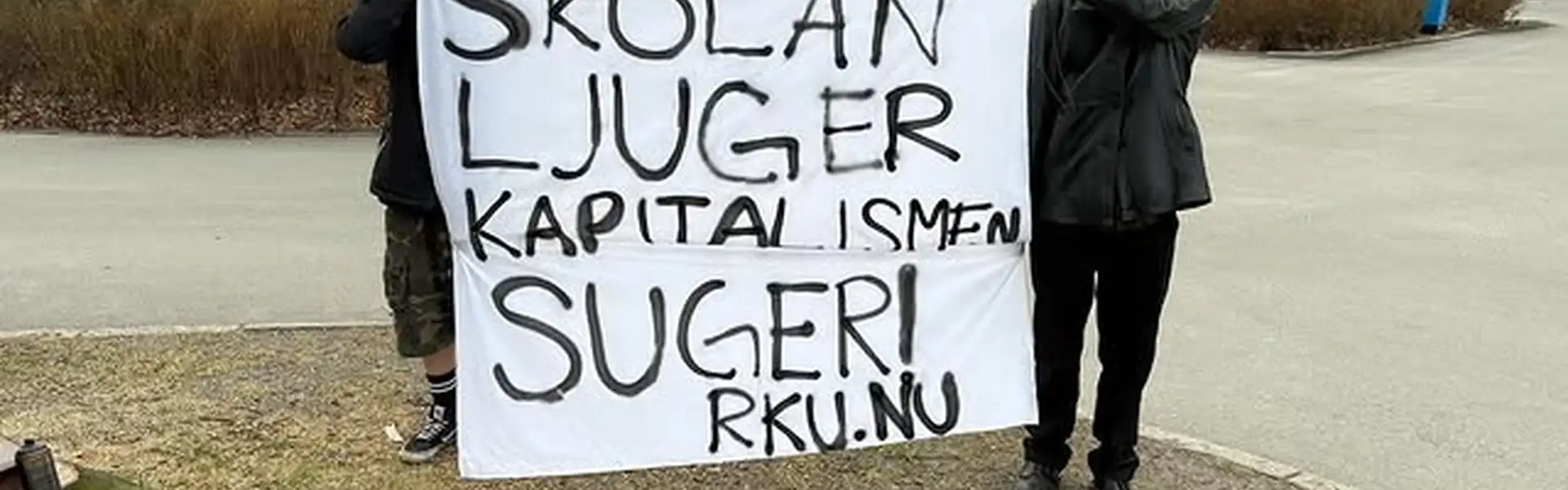 Bild p&aring; tv&aring; personer som h&aring;ller upp en banderoll d&auml;r det &auml;r sprejm&aring;lat "Skolan ljuger, Kapitalismen suger"