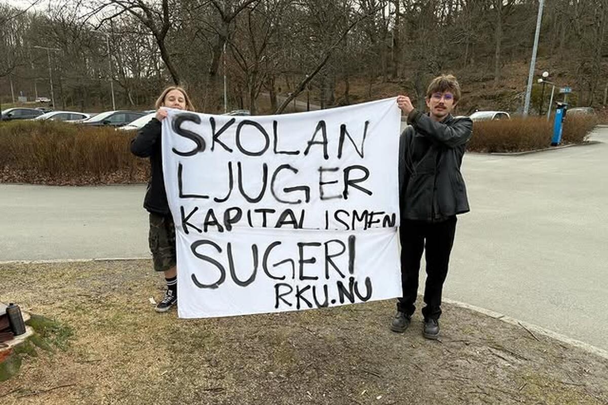 Bild på två personer som håller upp en banderoll där det är sprejmålat "Skolan ljuger, Kapitalismen suger"