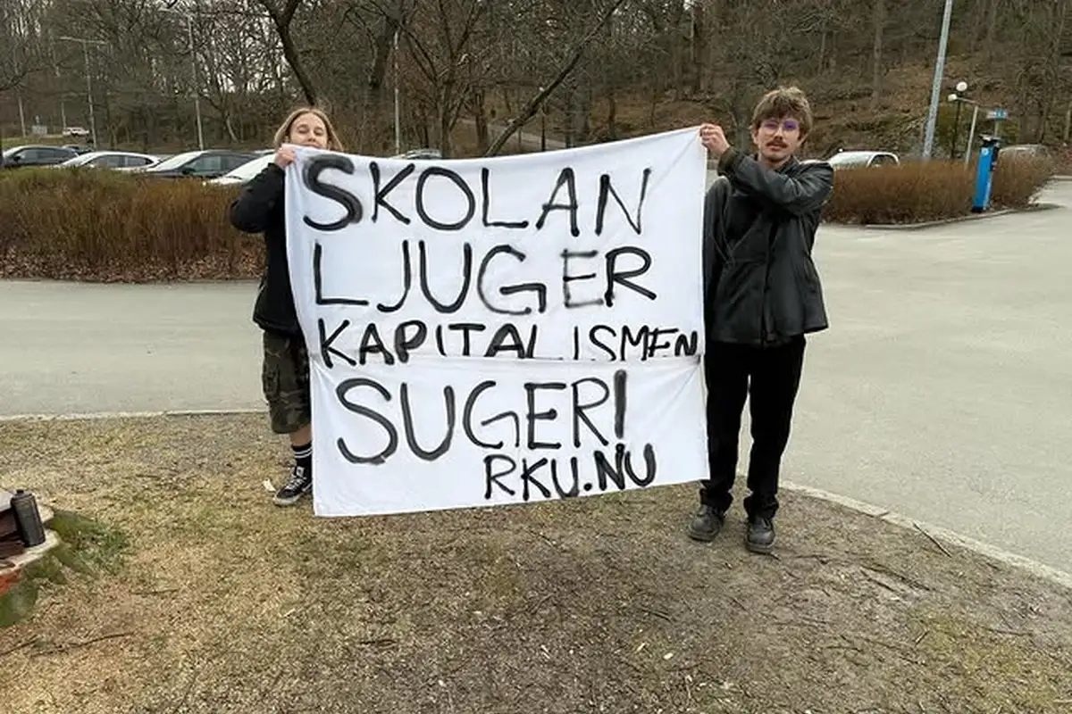 Bild p&aring; tv&aring; personer som h&aring;ller upp en banderoll d&auml;r det &auml;r sprejm&aring;lat "Skolan ljuger, Kapitalismen suger"